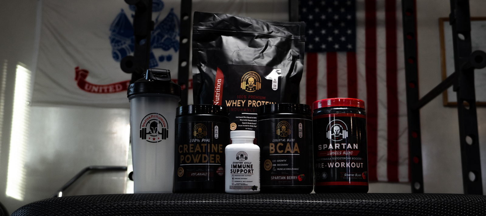 Spartan Supplement products and shaker bottle on top of gym bench at fitness gym.