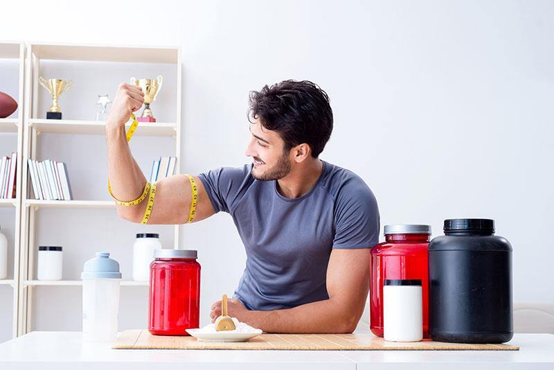 man with nutrition supplements flexing his arm with a measuring tape around his bicep 
