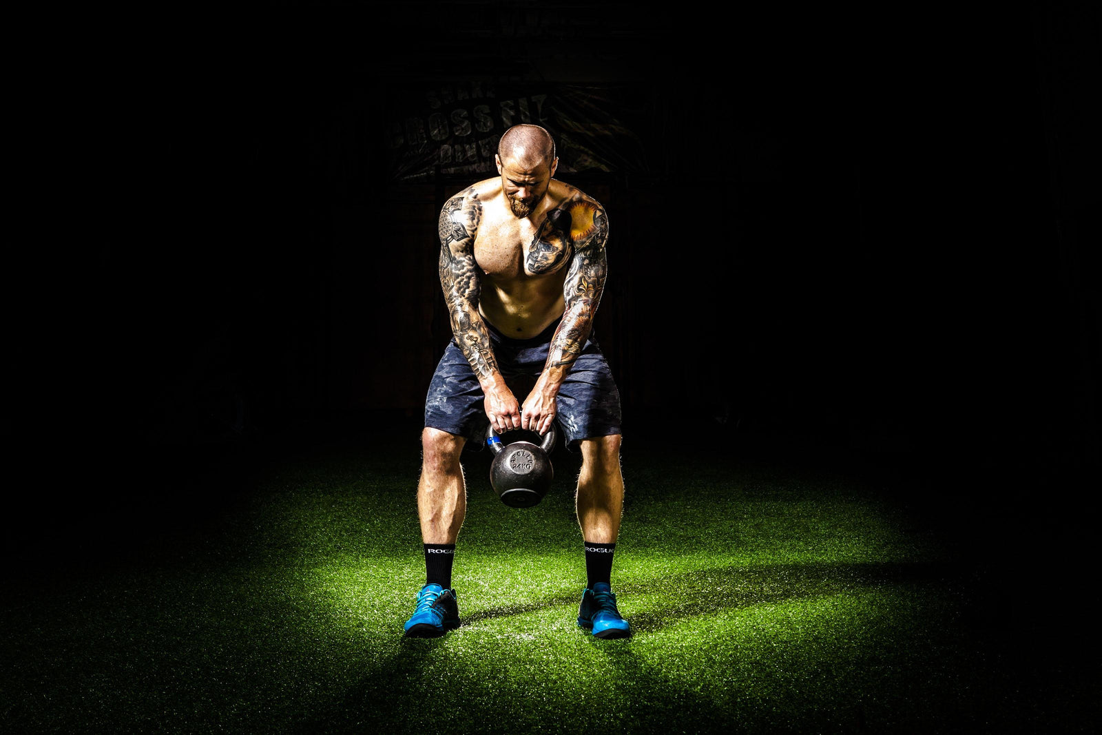 Physically fit man with tattoos working out with a kettle bell  