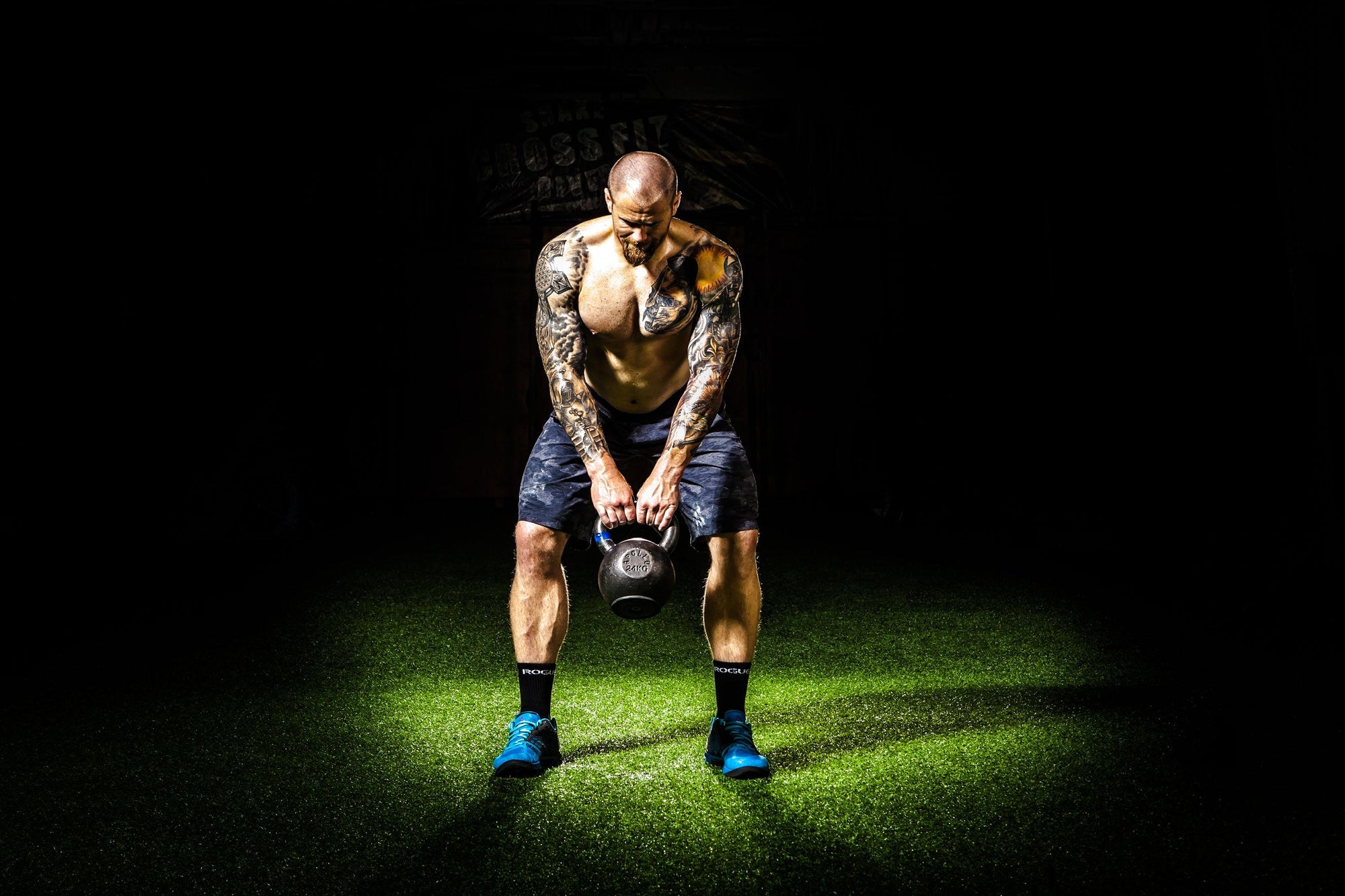 Physically fit man with tattoos working out with a kettle bell  